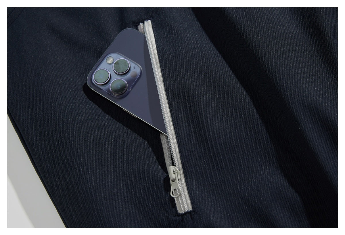 A smartphone tucked into a narrow light gray zippered pocket on dark navy garment fabric.