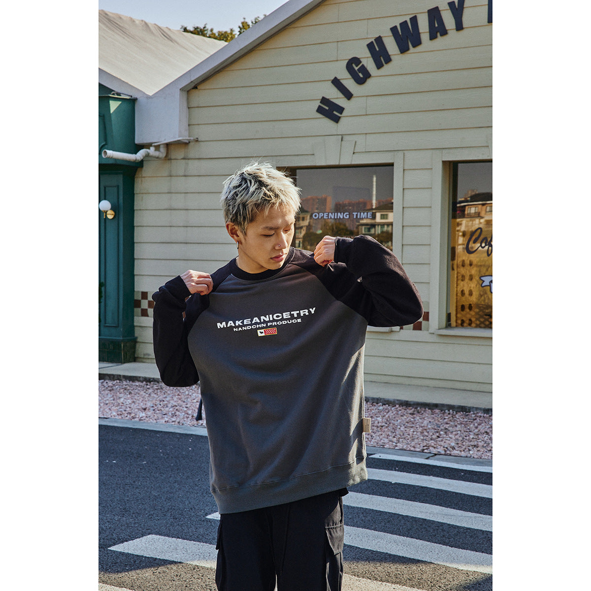 Model wearing a charcoal sweatshirt with black sleeves and a white chest graphic, shown from the front outdoors.