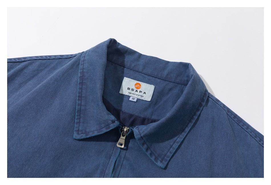 Close-up of a blue jacket's pointed collar, front zipper, and sewn neck label.