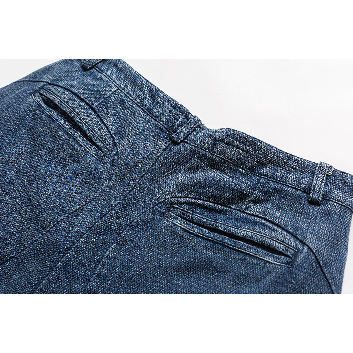 Close-up of blue trousers showing the waistband, belt loops, and two narrow welt pockets.