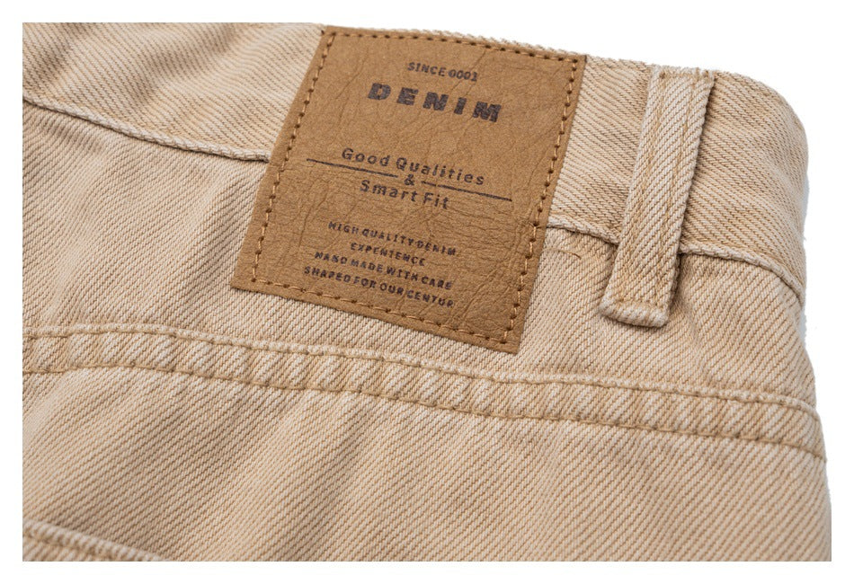 Close-up of the beige denim waistband with a brown sewn-on patch bearing English text.