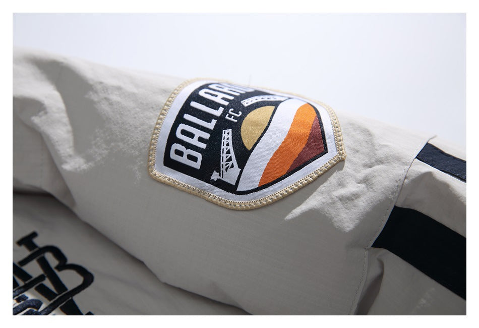 Close-up of an embroidered black, white, and orange shield patch on the off-white jacket sleeve.