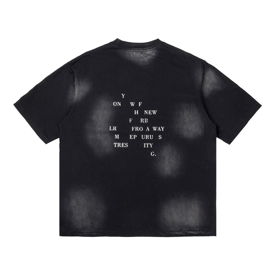 Back of distressed black t-shirt with faded gray spray marks and a scattered white letter print across the upper back
