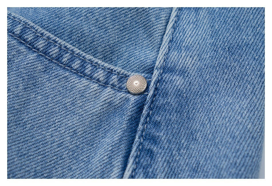 Close-up of light blue denim stitching and a small round metal rivet.