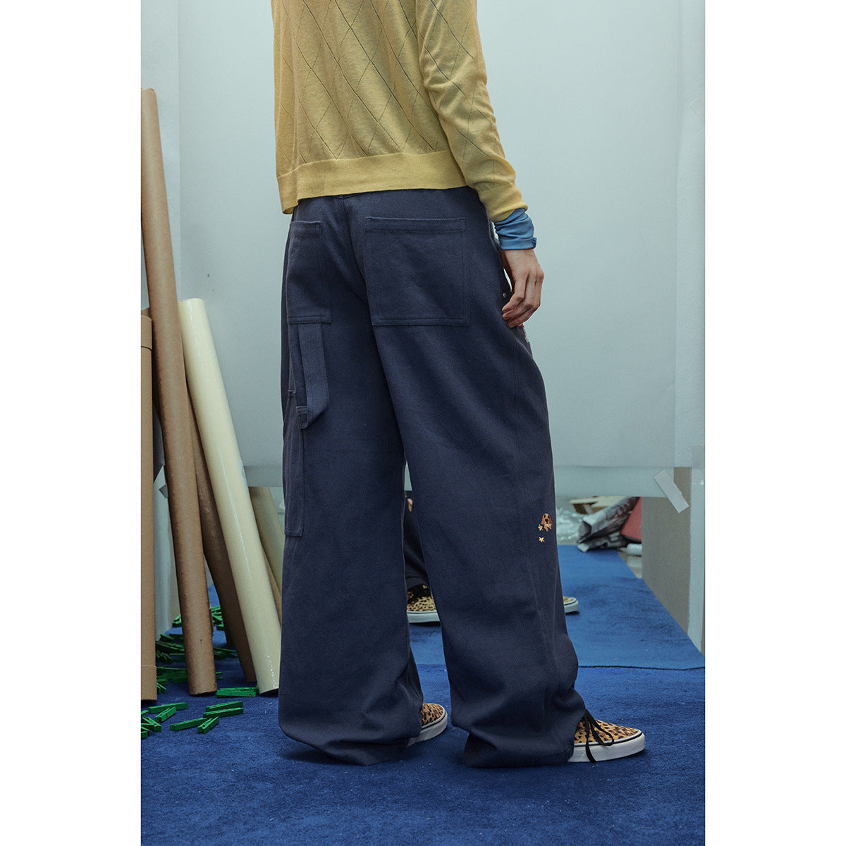Back view of a model wearing wide-leg navy cargo pants with large pockets and small embroidered motifs.