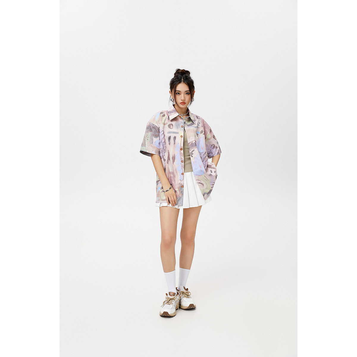 Model wearing an oversized pastel abstract-print short-sleeve button-up shirt with a chest pocket and white pleated skirt.