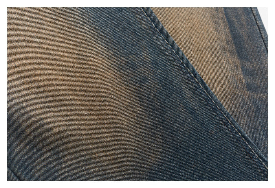 Close-up of blue denim with diagonal seam stitching and mottled tan fading.