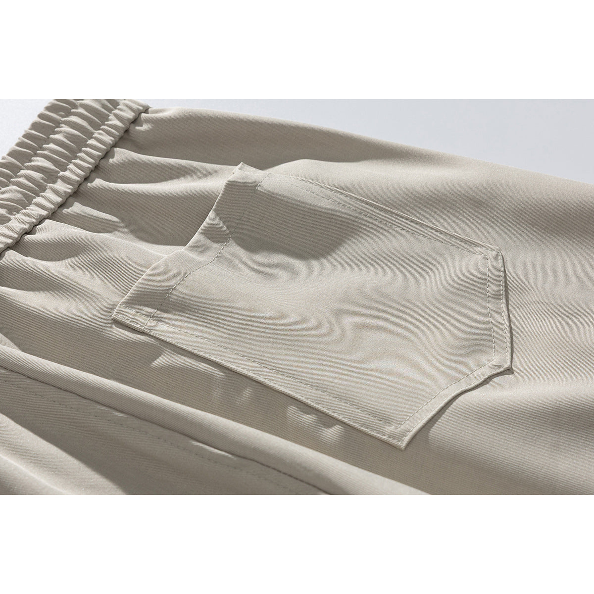 Close-up of light beige trousers showing the gathered waistband and a stitched patch pocket.