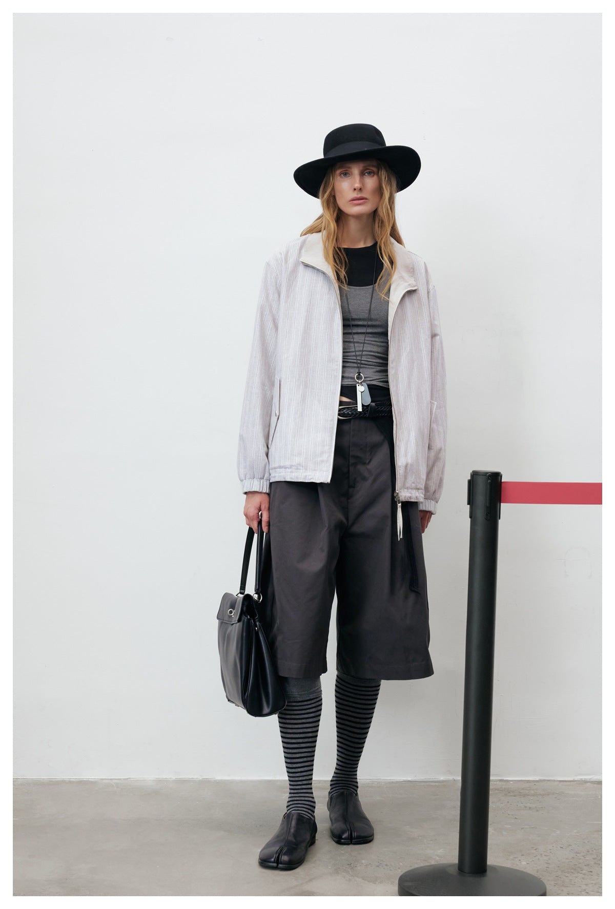 Front view of a model wearing an open light gray pinstriped zip jacket over a dark outfit.