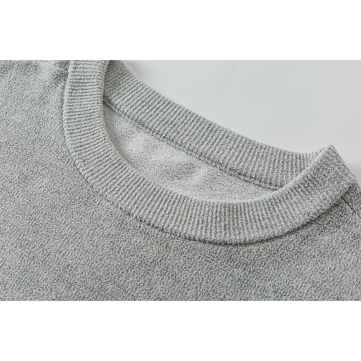 Close-up of a light gray sweater’s ribbed crew neckline and knit texture.