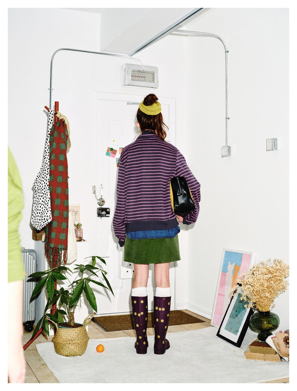 Back view of a model wearing a purple-and-black striped jacket over a denim shirt and green skirt.