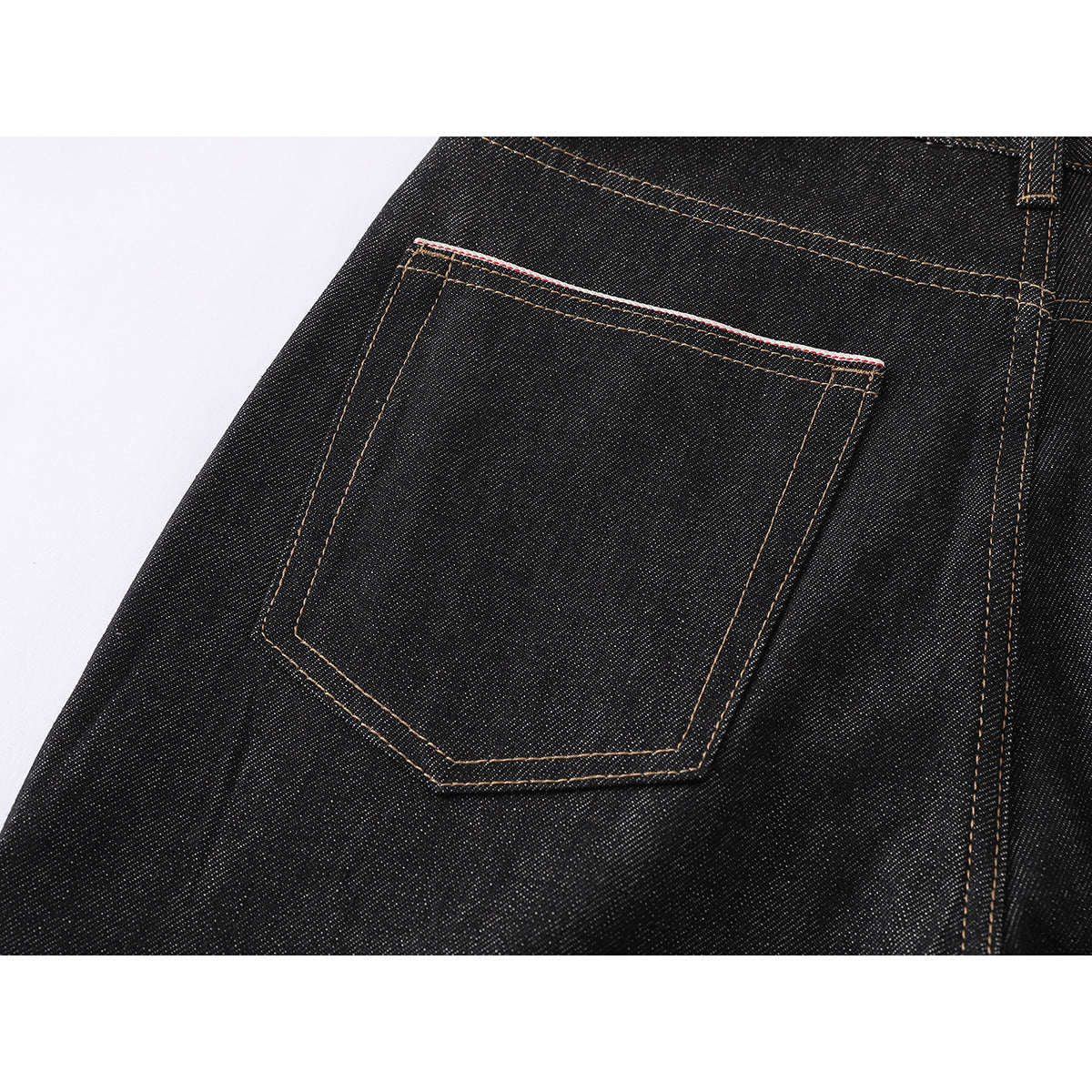 Close-up of a back patch pocket on black jeans, with tan stitching and a narrow red-and-white edge.