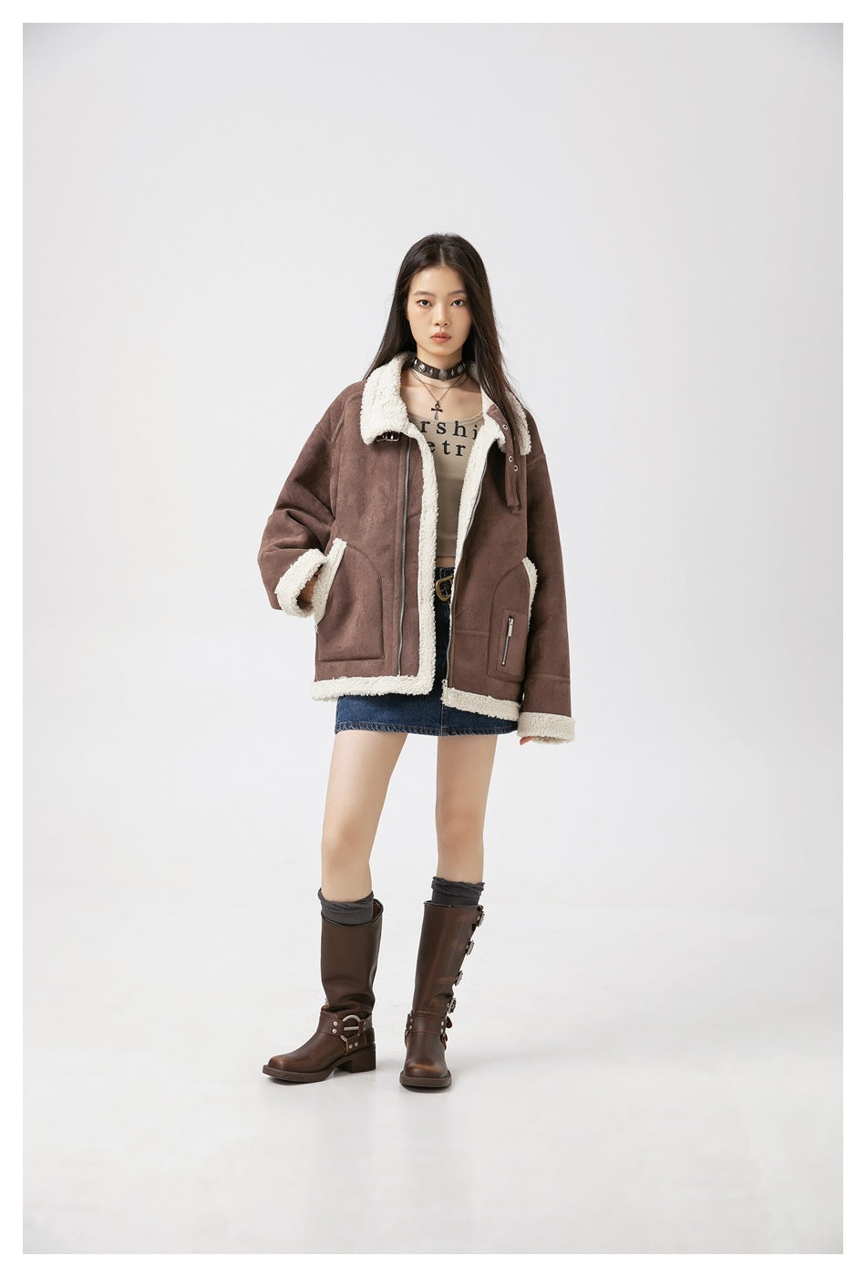Model wearing the brown fleece-trimmed jacket open over a cropped top, denim mini skirt and brown tall boots