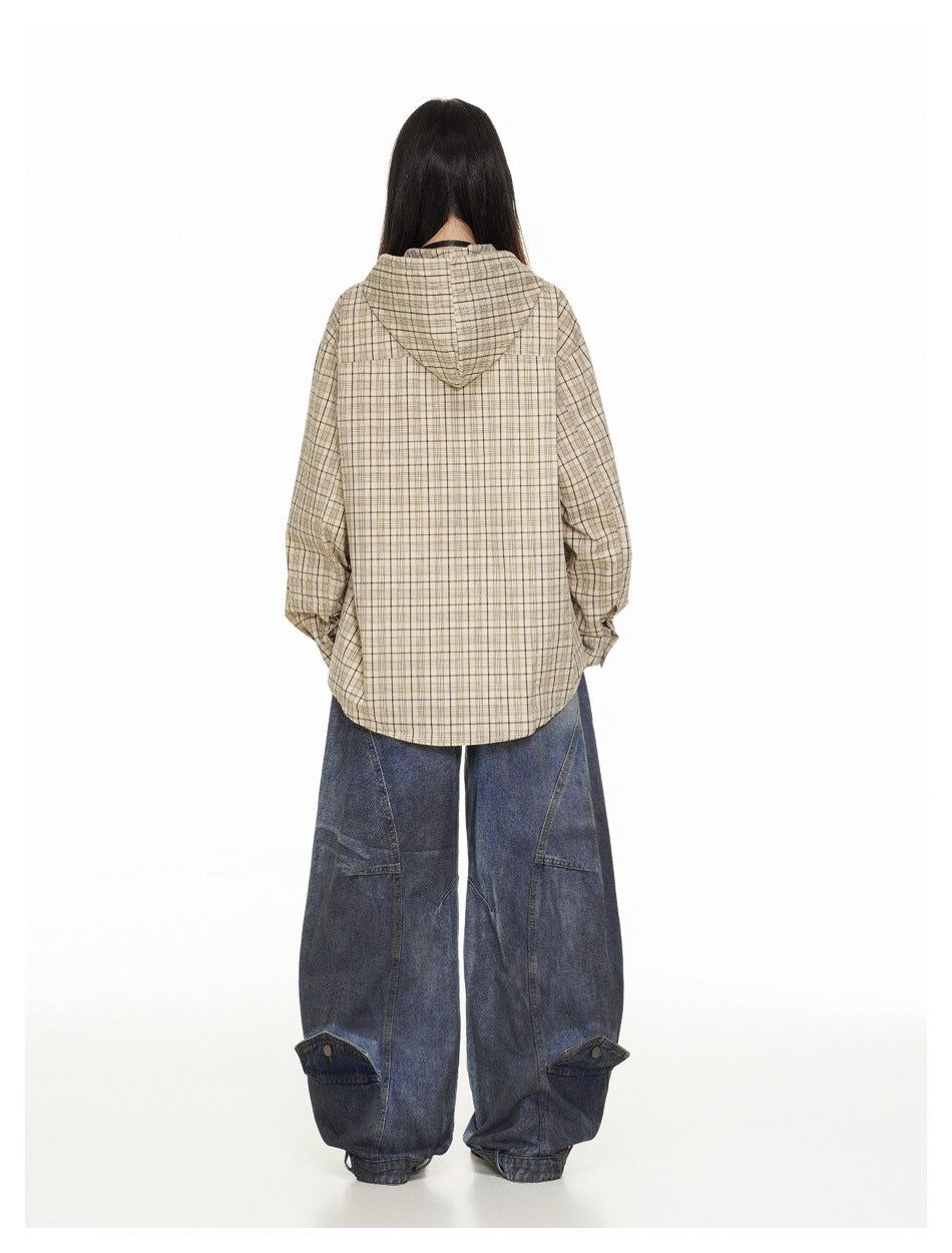 Back view of a model wearing a beige plaid hooded shirt jacket with oversized dark blue jeans.