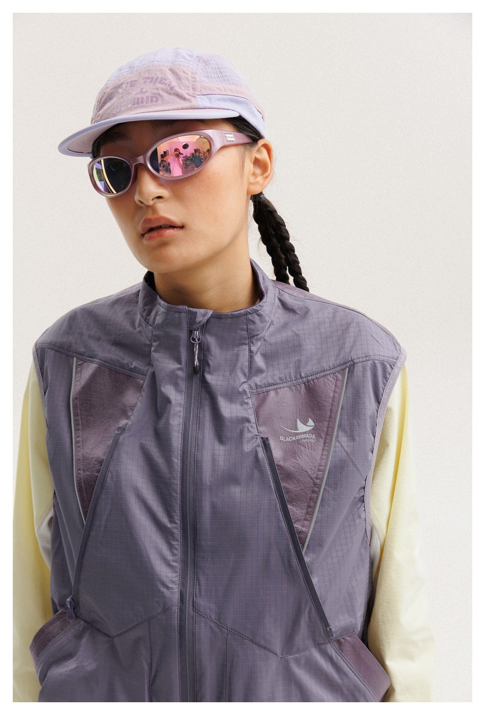 Close-up of a lavender-gray utility vest with zip pockets and a small chest logo, worn over a pale top.