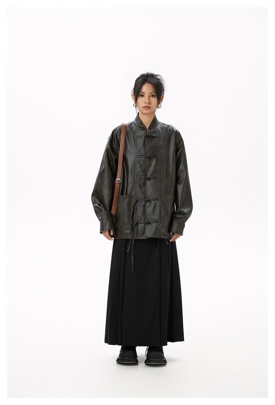 Model faces forward in a dark toggle-front jacket with long ties, a black skirt, and a brown shoulder bag.