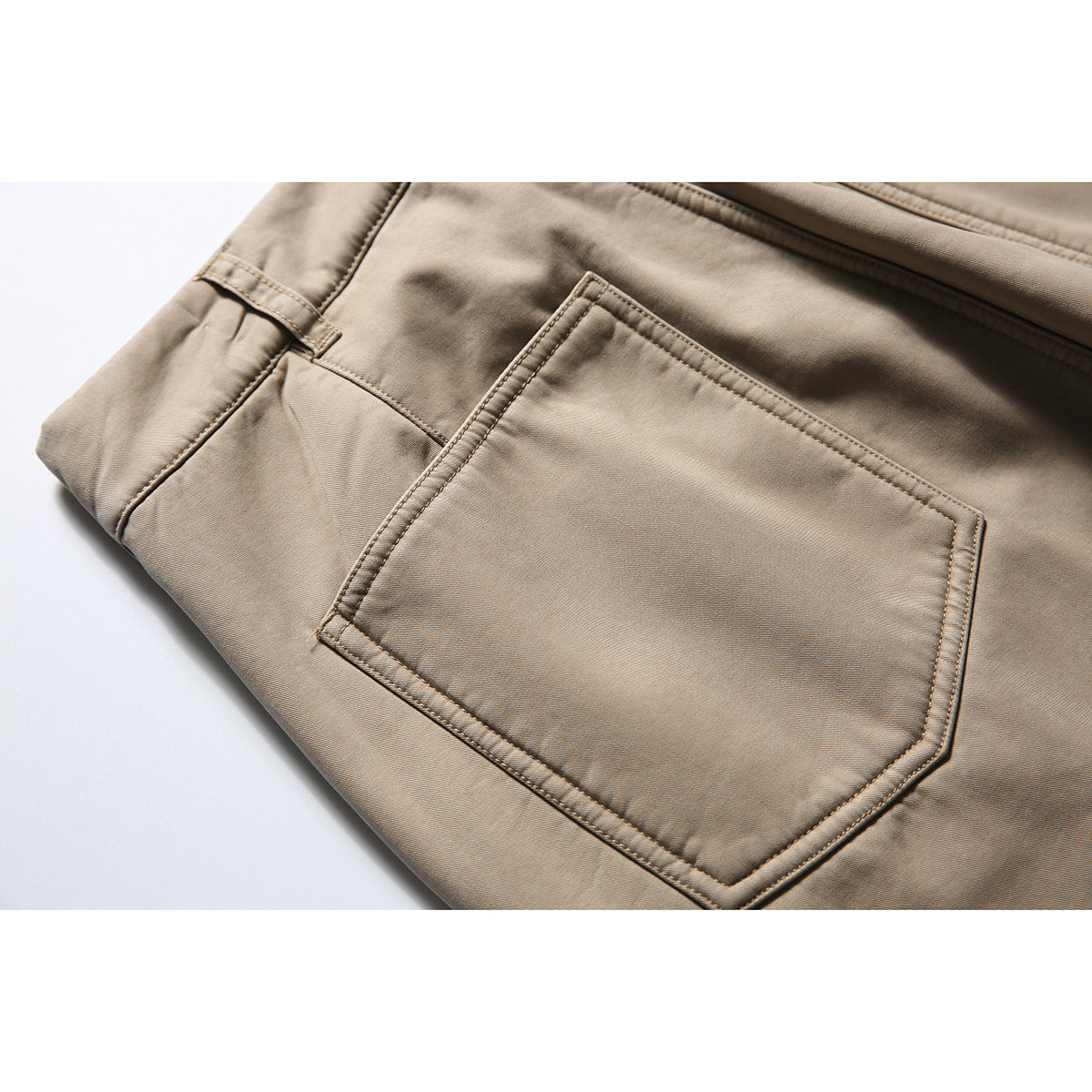 Close-up of beige trousers showing a stitched rear patch pocket and waistband seam.