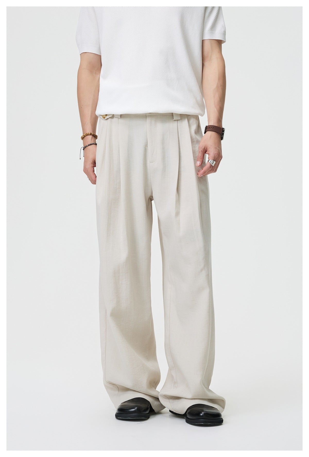 Close front view of loose ivory trousers worn with a white top, showing pleats, belt loops, and wide legs.