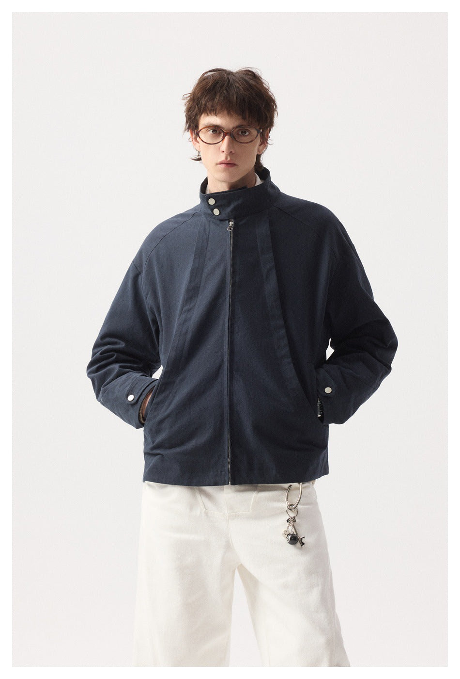 Front view of a model wearing a navy zip jacket fastened to its stand collar, with white trousers.