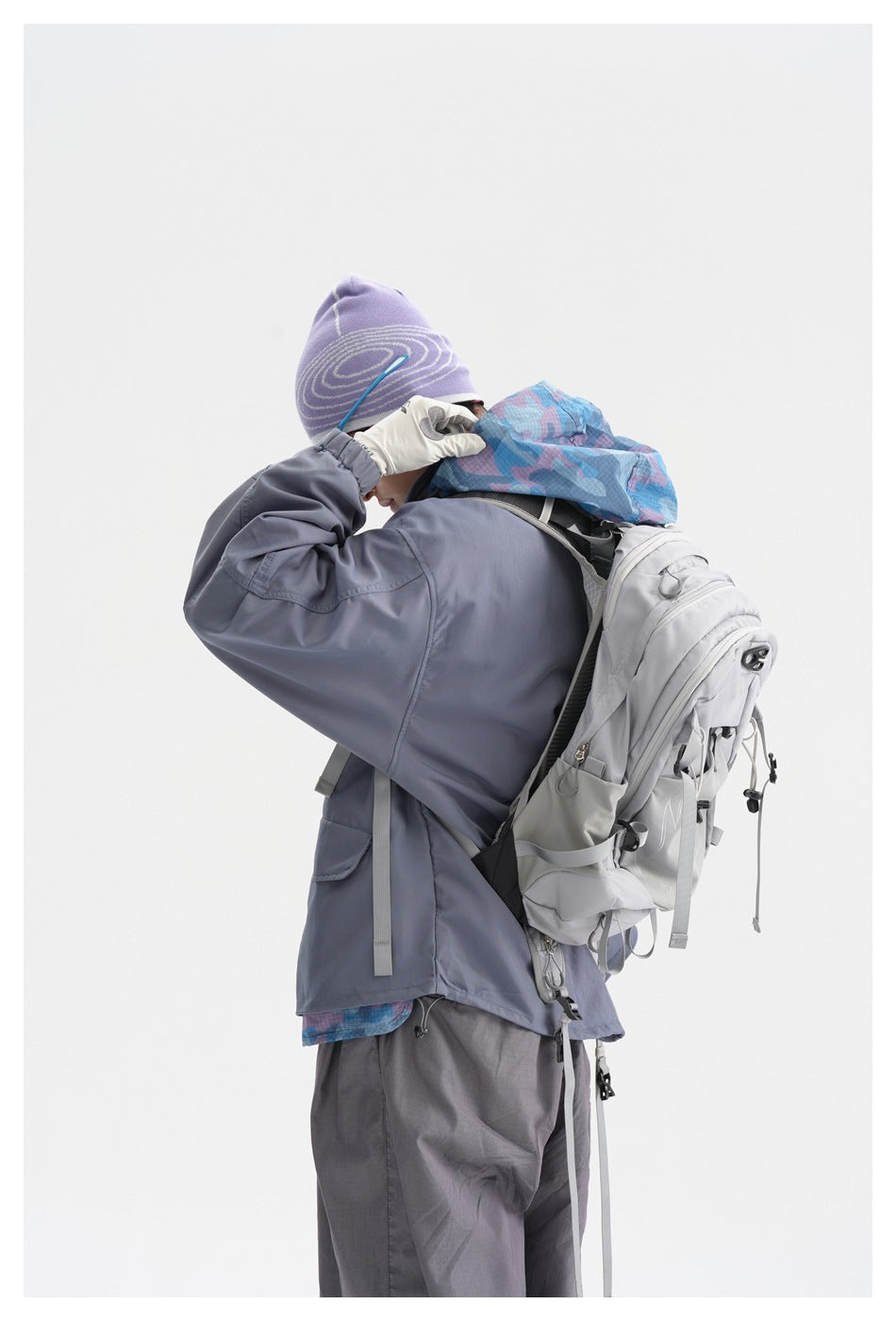 Side view of a model in a slate gray hooded jacket with blue patterned lining and a large light gray backpack.
