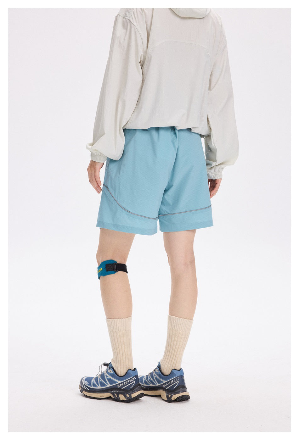 Rear view of a person wearing light blue shorts with curved gray piping and wide hems.