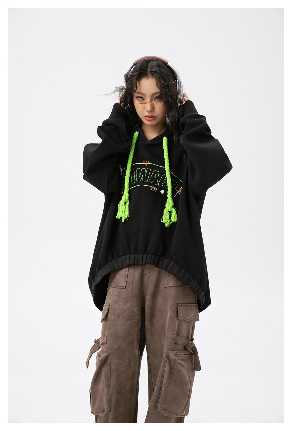 Closer view of a model in an oversized black hoodie with neon green braided drawstrings and brown cargo pants.