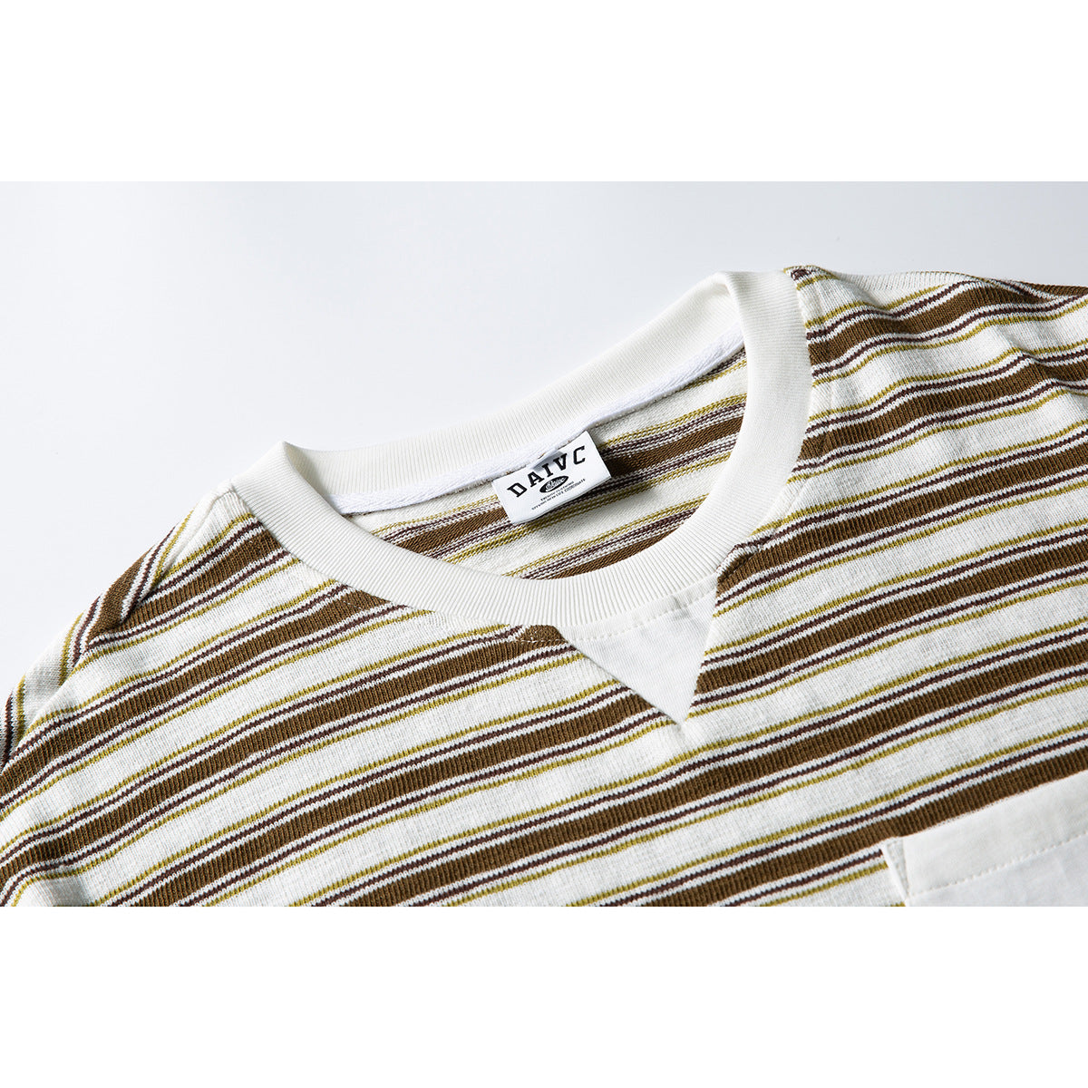 Close-up of a cream T-shirt with brown and olive stripes, showing the ribbed neckline, V insert, and chest pocket edge.