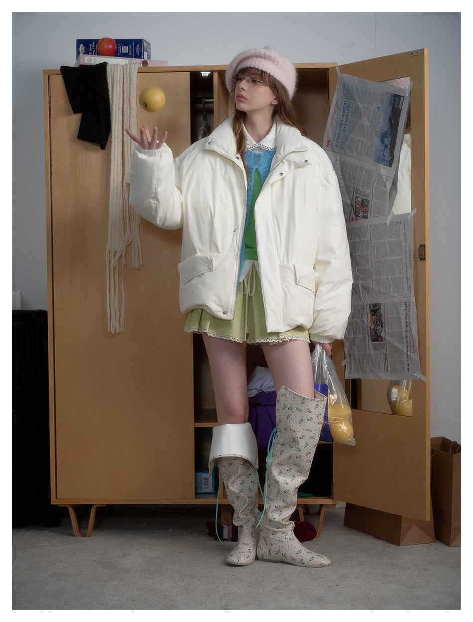 Model wearing a white puffer jacket over a blue cardigan and green skirt, standing by a wooden wardrobe