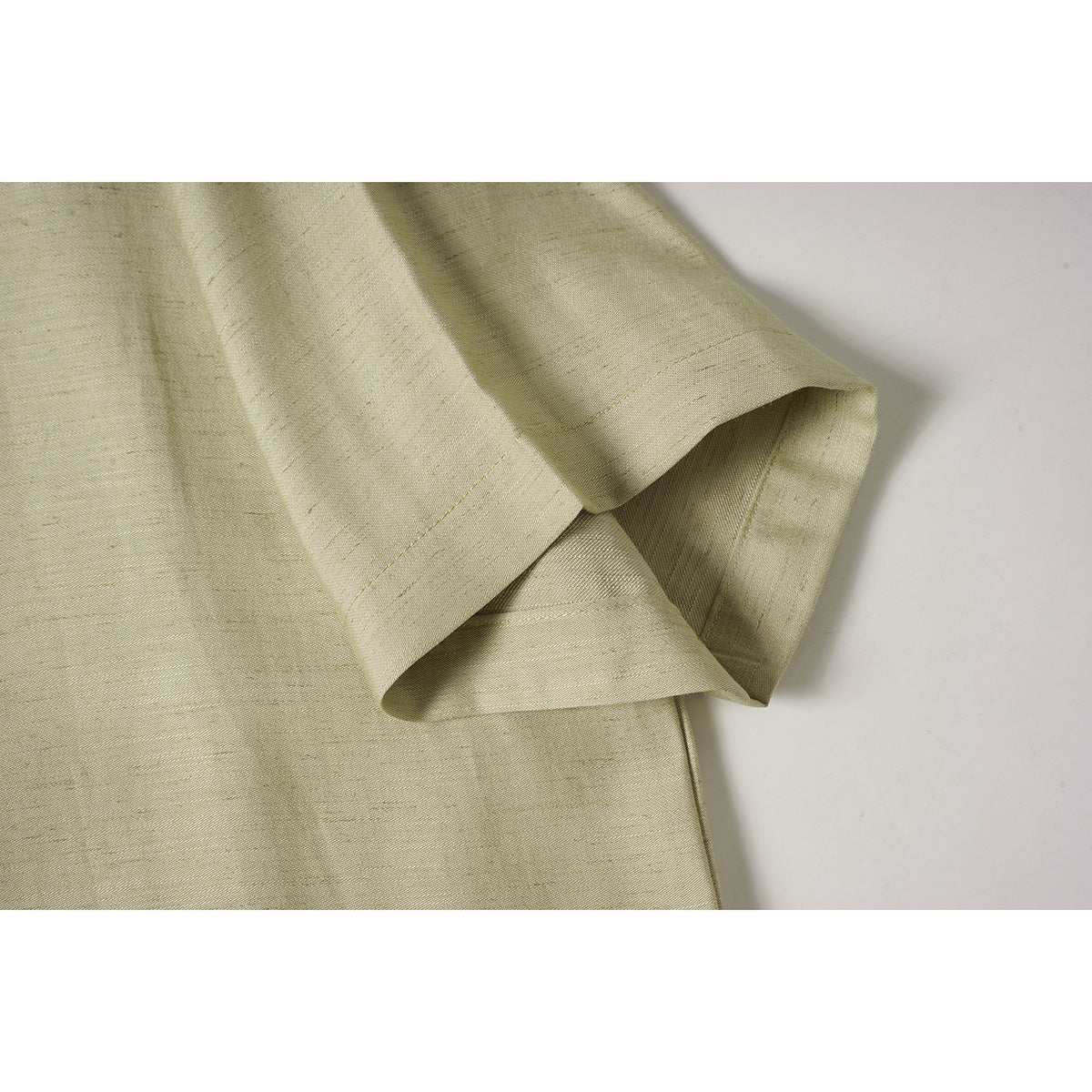 Close-up of the pale beige shirt's short sleeve and stitched hem.