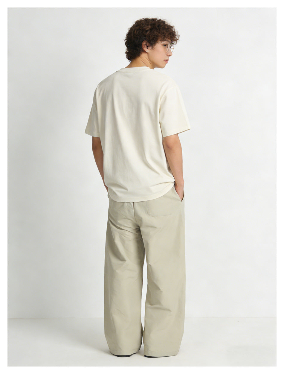 Model wearing a light beige T-shirt and wide-leg trousers, shown from the back.