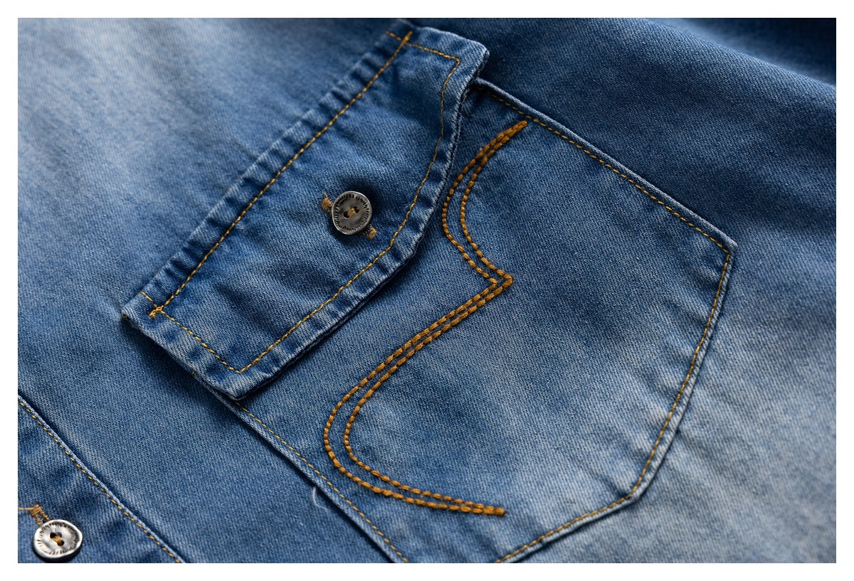 Close-up of a blue denim shirt chest pocket, flap, metal buttons, and tan contrast stitching.