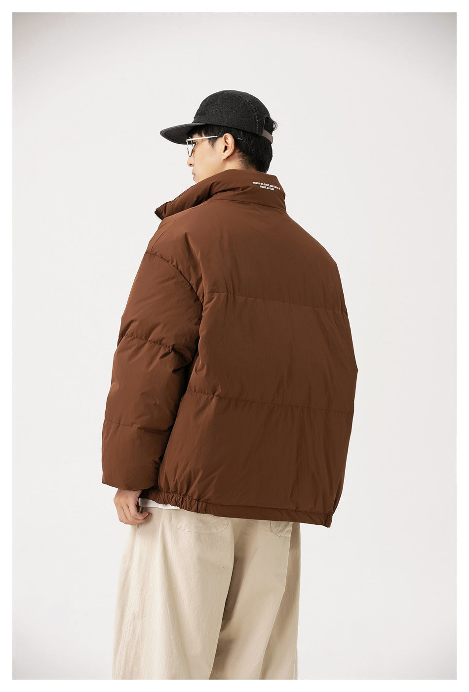 Rear view of a person wearing a brown padded jacket with a high collar and cream trousers.