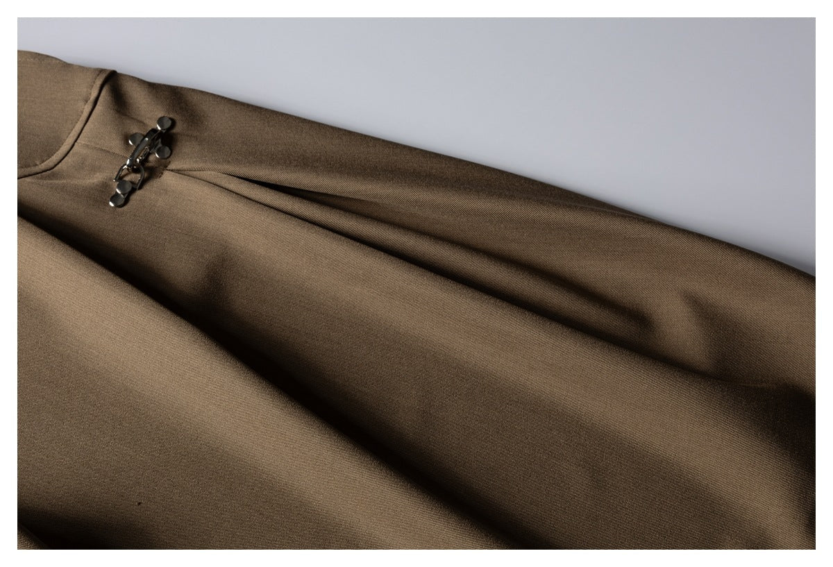 Close-up of brown trouser fabric and pleats beside the metal clasp closure.