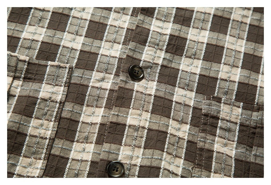 Close-up of the brown, beige and gray plaid shirt front, showing buttons, placket and a stitched pocket edge.
