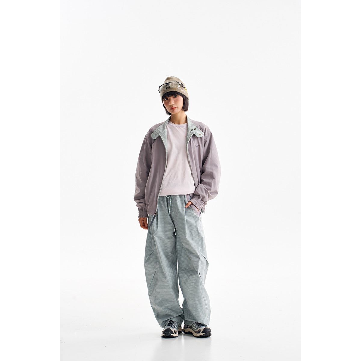 Model wearing a muted lavender zip jacket, white shirt, and loose pale blue-gray trousers.
