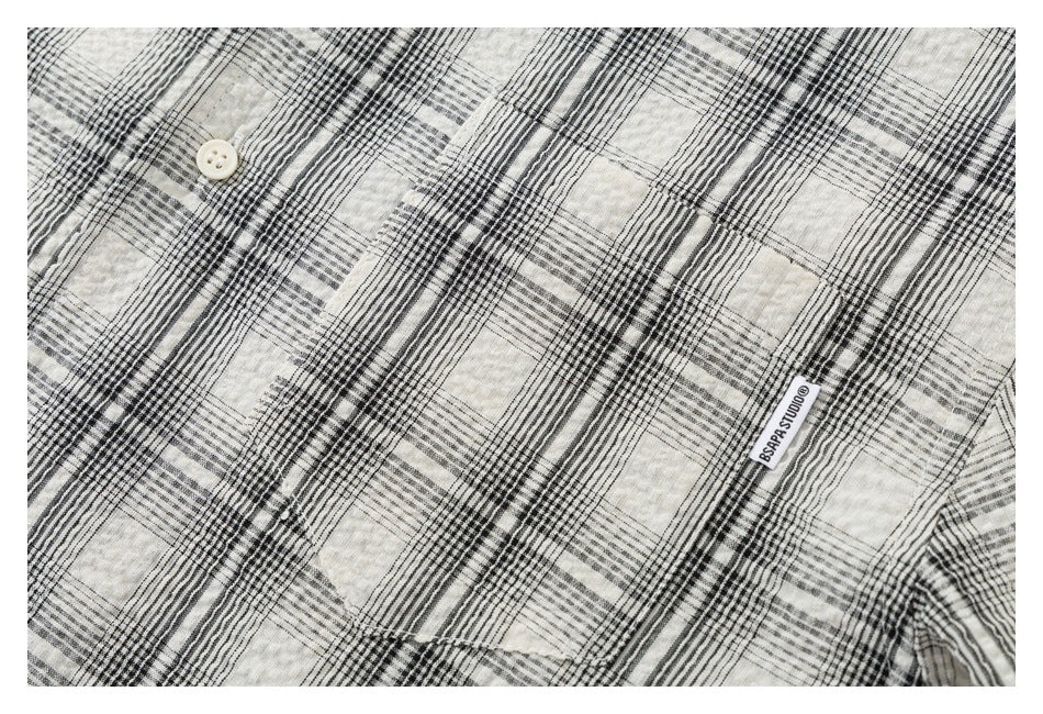 Close-up of a cream and black plaid shirt with a white woven label reading “DSRAP STUDIOS.”