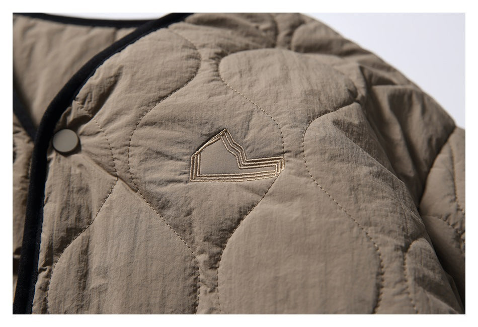 Close-up of the taupe jacket’s quilted stitching, snap, and small embroidered outline emblem.