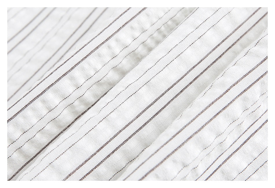 Close-up of white textured fabric with narrow parallel dark gray and brown pinstripes.
