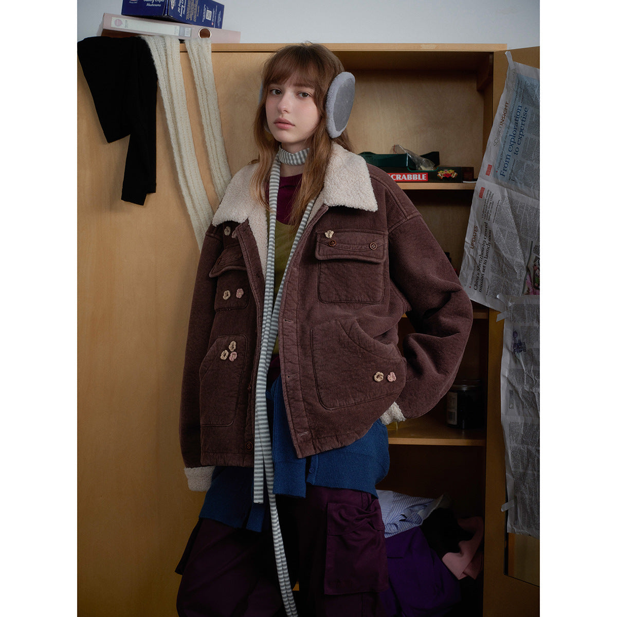 Closer view of a model wearing a brown jacket with a cream collar, cuffs, multiple pockets, and floral accents.