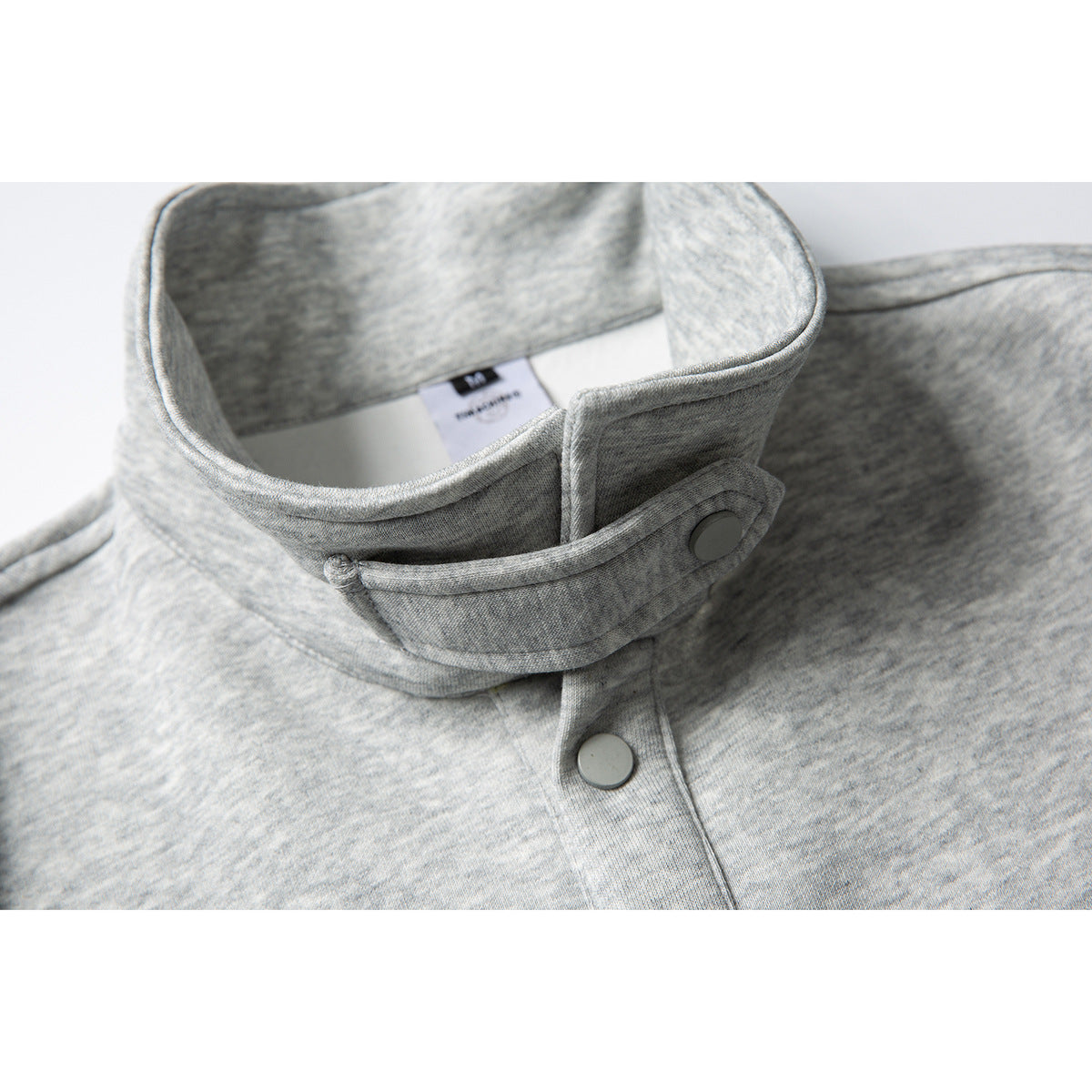 Close-up of the raised collar and snap-button tab on a light heather-gray polo shirt.