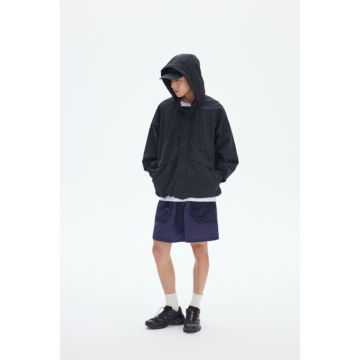 Model wearing a black hooded jacket, dark navy shorts, white socks and black sneakers.