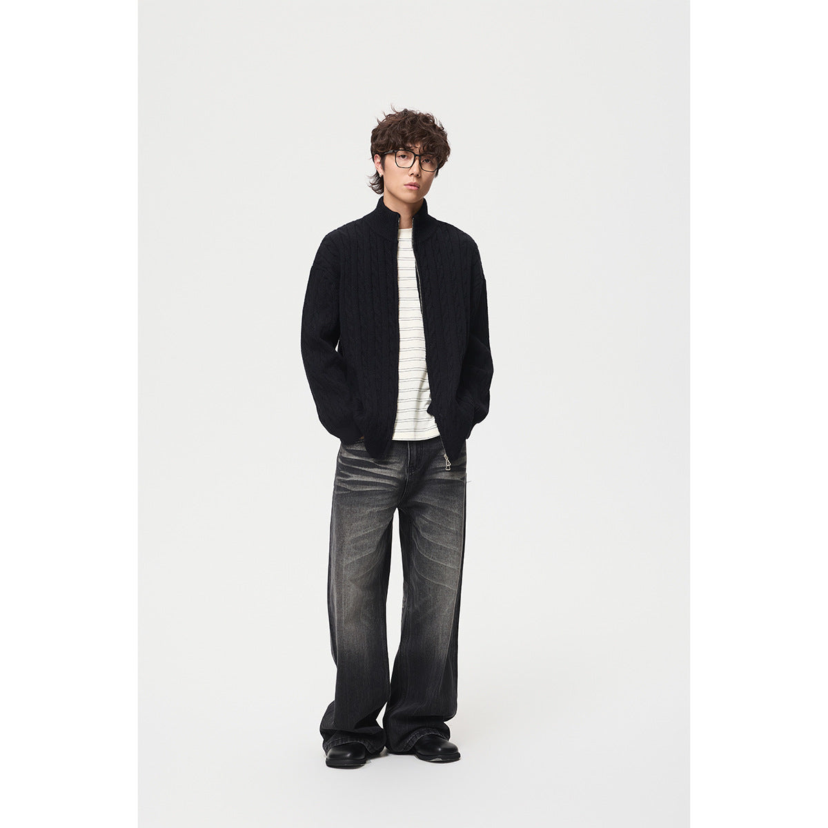 Full-length model wearing a black cable-knit zip cardigan over a striped shirt and dark wide-leg jeans.