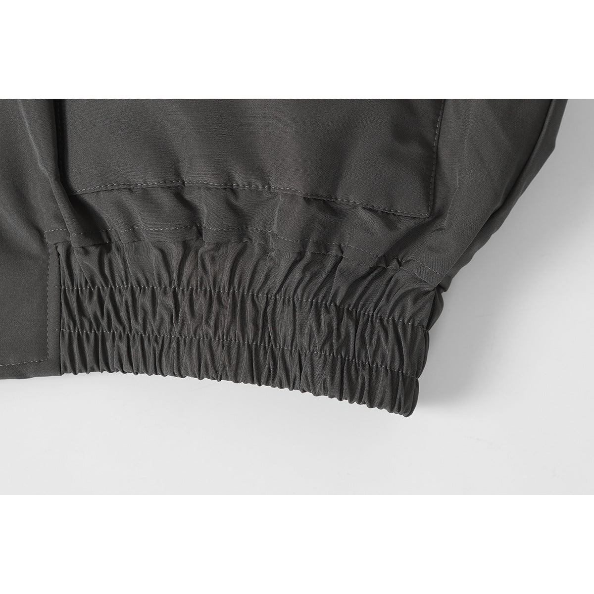 Close-up of the charcoal jacket's gathered elastic hem and stitched panel seams.