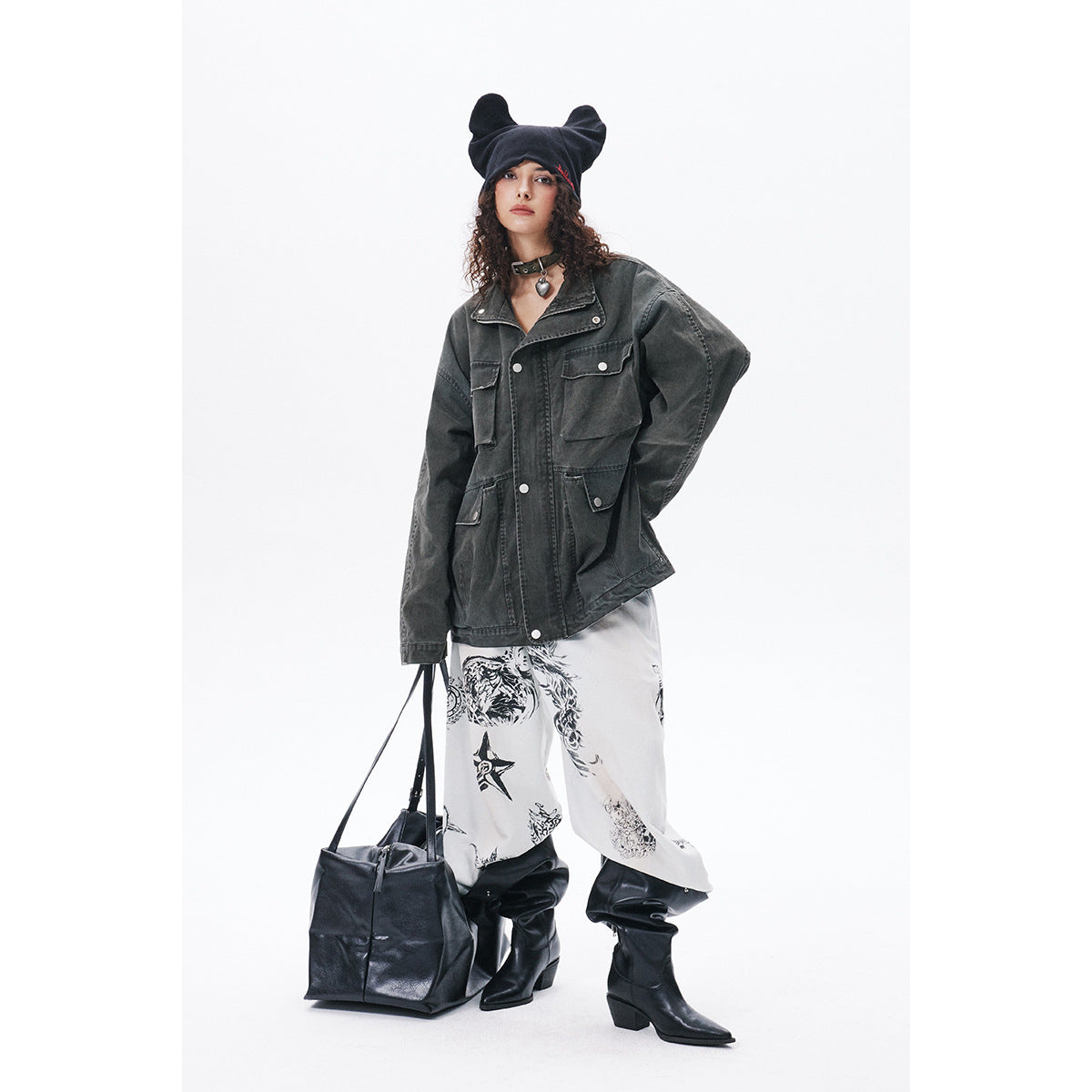 Full-length model wearing a charcoal utility jacket and printed white pants with black boots and a beanie.