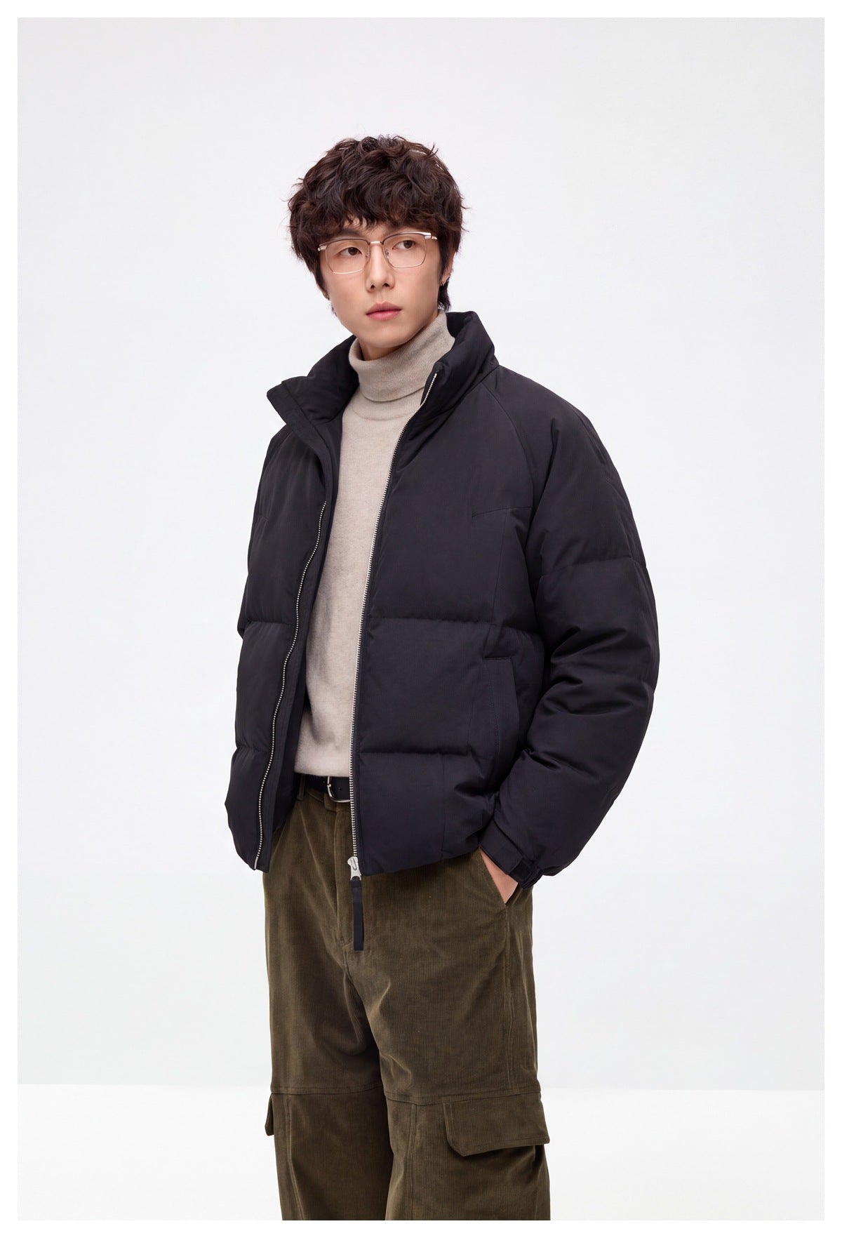 Model wearing an open black padded jacket with a raised collar and horizontal quilting, over a beige turtleneck.