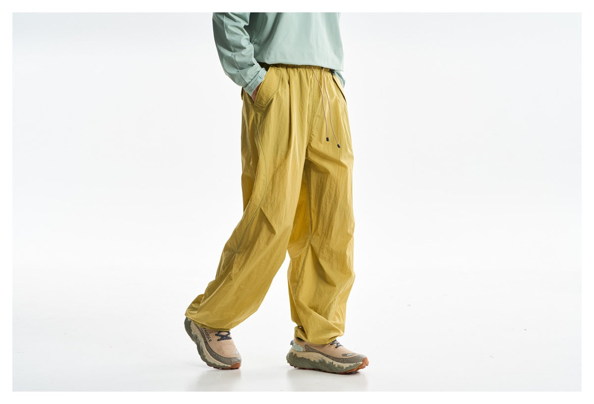 Cropped side view of a model wearing loose mustard-yellow trousers with an elastic waist, drawstring, and side pocket.