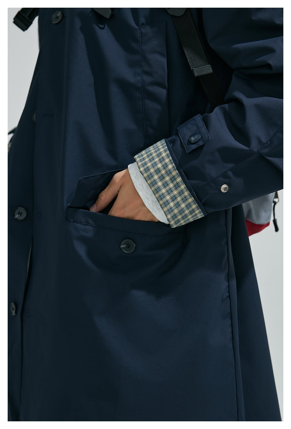 Close-up of a navy coat showing its buttoned front, large pocket, adjustable cuff, and checked lining.