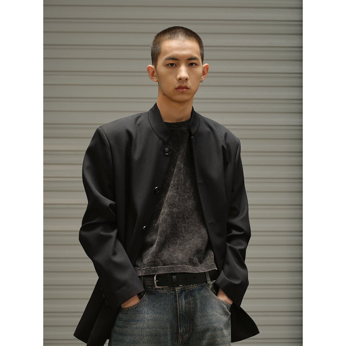 Closer view of a model wearing a black button-front band-collar coat over a dark washed top and faded denim shorts.