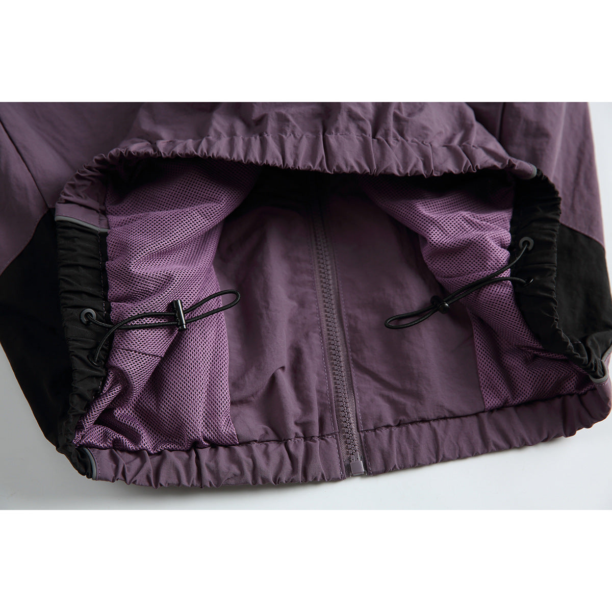 Close-up of the plum jacket's open lower hem, showing purple mesh lining, a central zipper, and adjustable drawcords.