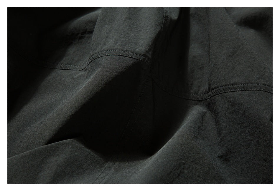 Close-up of black fabric with curved double-stitched seams and gathered folds.